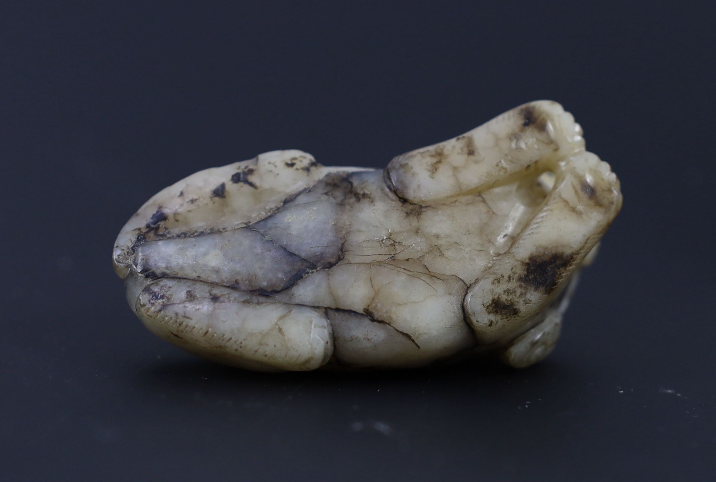 A Chinese Ming white and black jade figure of a recumbent beast, 6.8 cm long